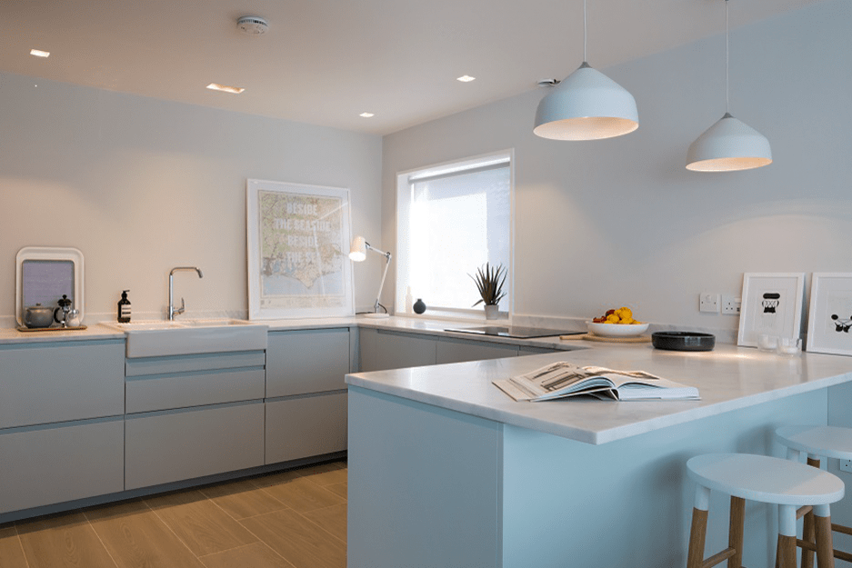 Modern kitchen with light blue cabinets, white countertops, and pendant lights.